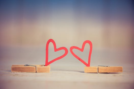 Two wooden clothespins with red heart shapes, symbolizing love and romance, on a blurred background.